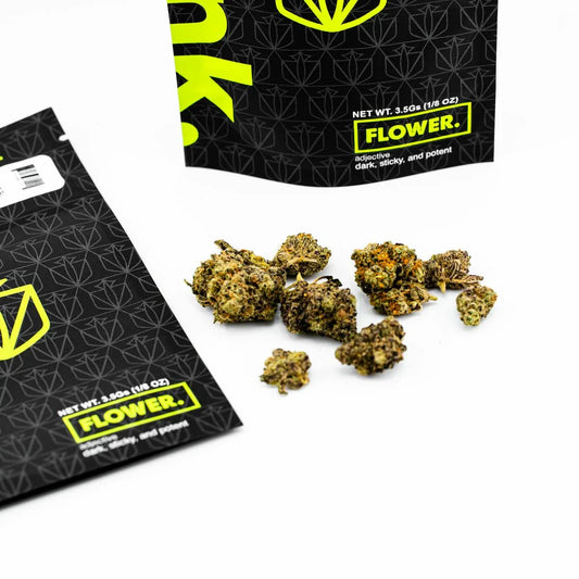 Cannabis flower buds displayed with black and neon green 3.5g packaging labeled 'FLOWER.' on white background